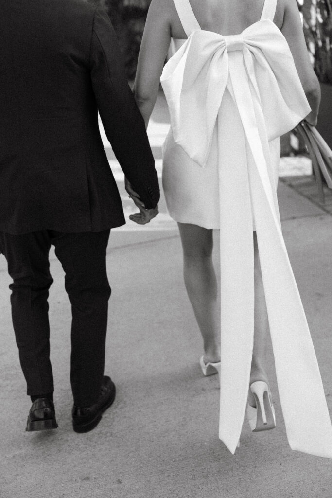 bride and groom walking away from camera, big white bow on brides dress, black and white photo 